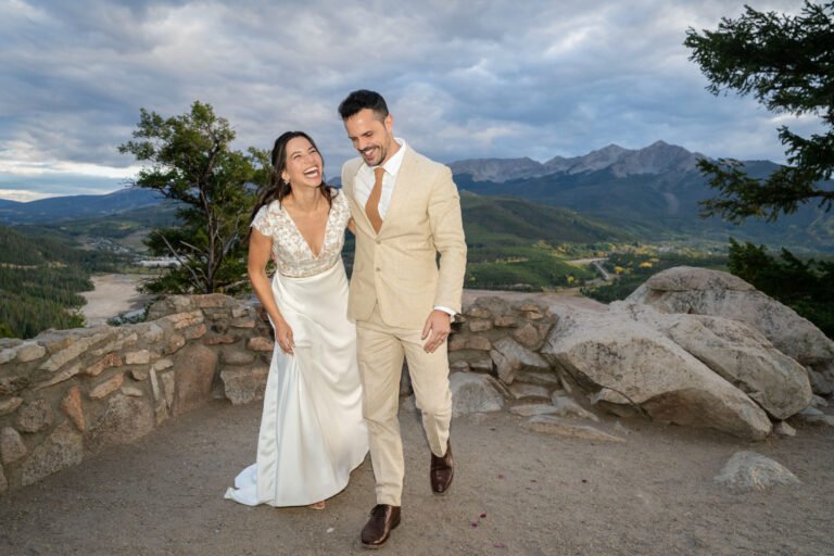 Alex and Nicole laugh together at a mountain overlook on their wedding day.