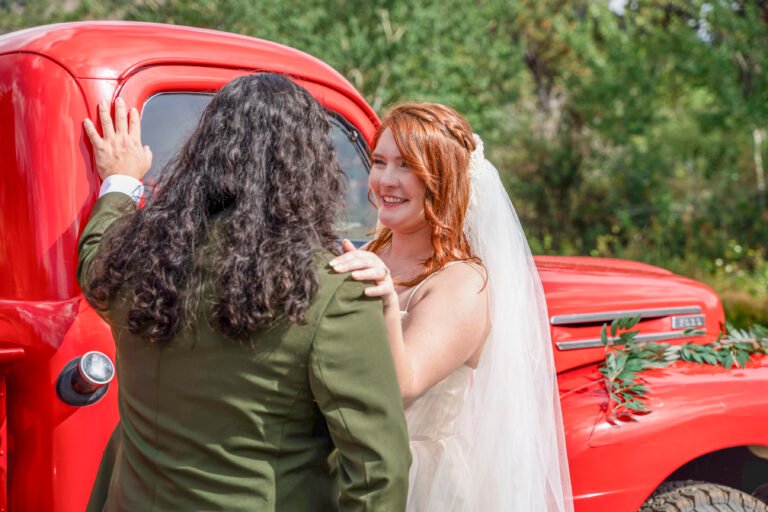 SEO filename Alt text 01-vince-ash-wedding-couple-portrait-red-vintage-truck.jpg Ash smiles at Vince as they embrace beside a red vintage truck on their wedding day.