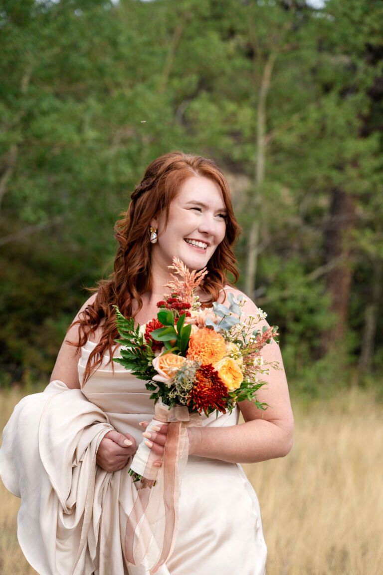 Ash smiles while holding a colorful bridal bouquet in an outdoor meadow.