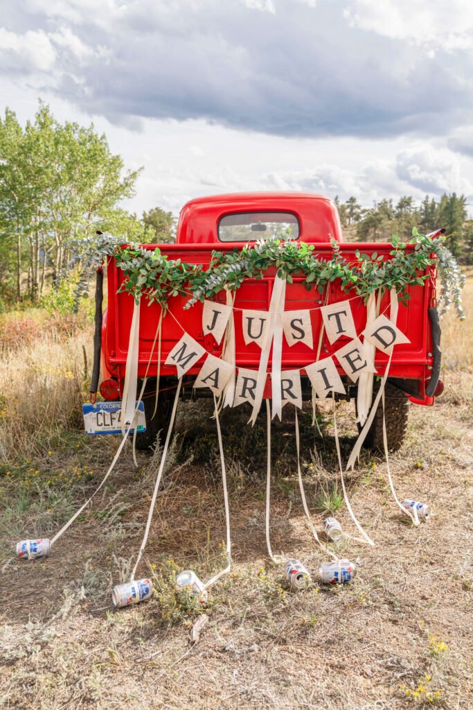 A red vintage truck decorated with greenery, a Just Married banner, and trailing cans.