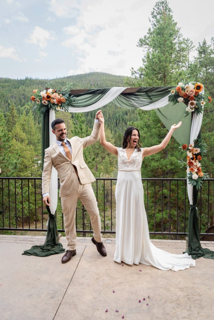 Alex and Nicole raise their joined hands in celebration after their outdoor wedding ceremony.