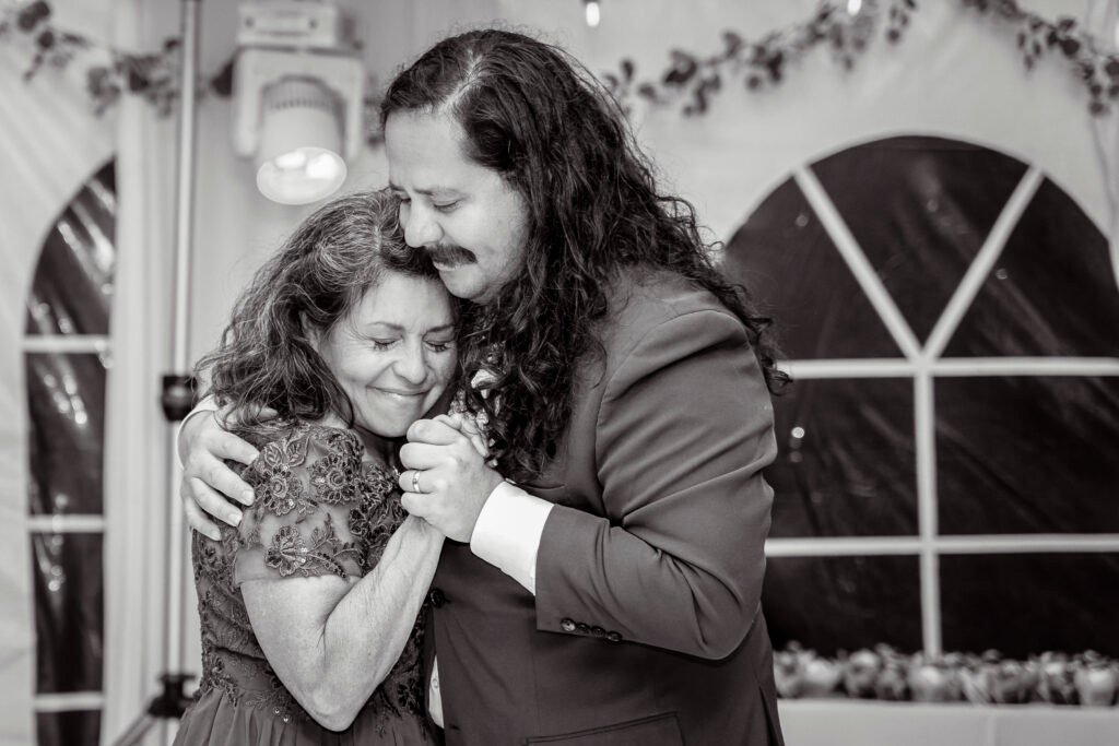 Black and white photograph of Vince embracing a loved one during a family dance at the wedding reception.