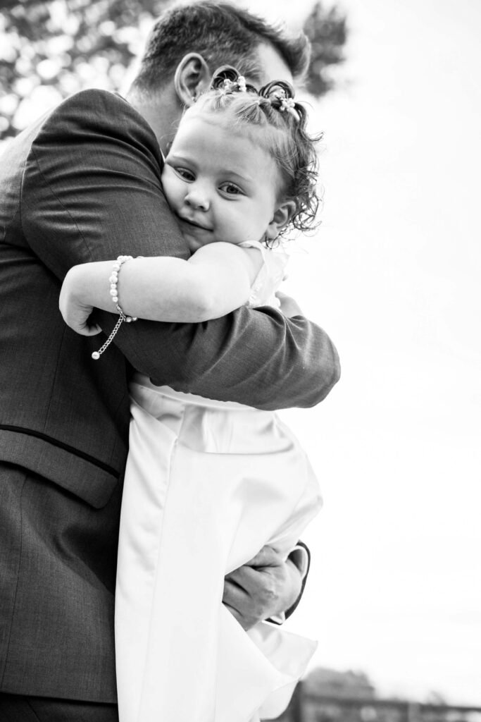 Black and white photograph of Michael hugging a flower girl before the ceremony.