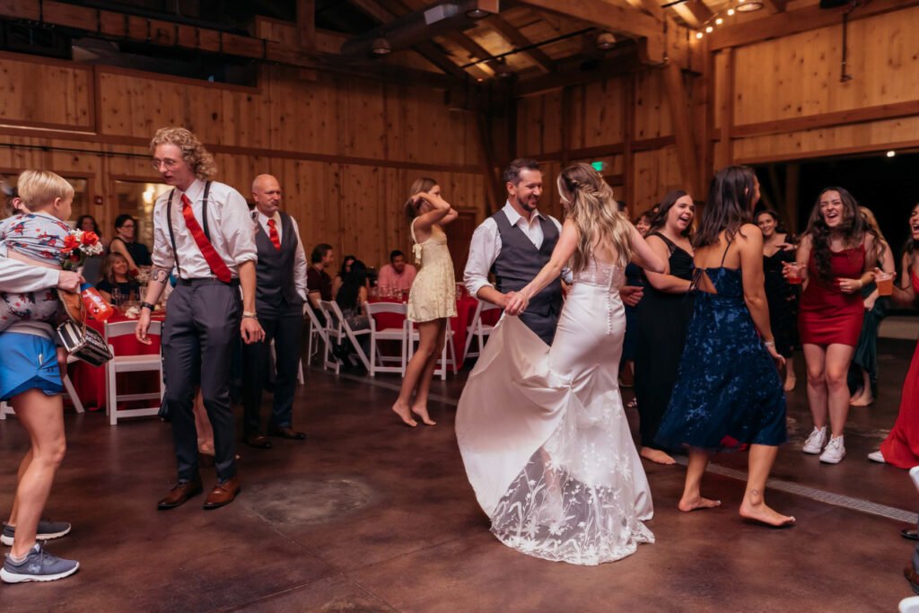 Leslie dances with guests during the reception in a rustic winery hall.